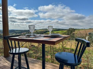 A wooden table with two chairs on a deck, overlooking a rural landscape with fields and a cloudy sky. - Cabana com Jacuzzi e Churrasqueira - Ibi na SP (Ibiuna)
