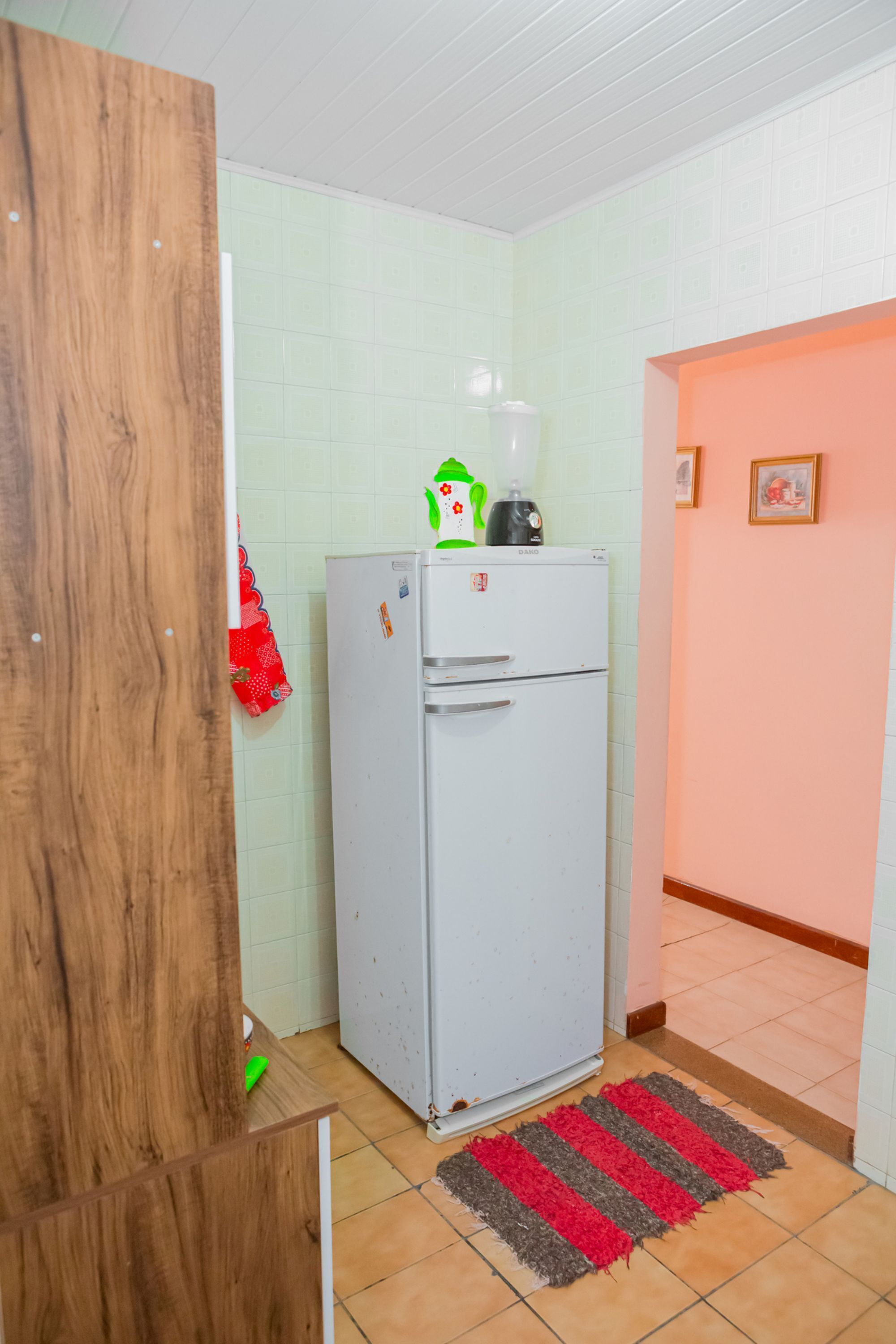 Une cuisine de taille modeste, avec un réfrigérateur blanc, une porte en bois et un tapis rayé rouge et gris sur le sol.
