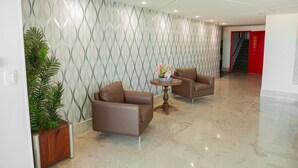 Un vestíbulo moderno con dos sofás de cuero marrón, una mesa redonda con un centro de mesa floral y una planta en maceta.