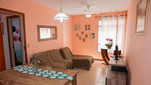 Una sala de estar acogedora con un sofá, una mesa de comedor con una jarra de vidrio y posavasos, y un mueble para televisión con un jarrón.