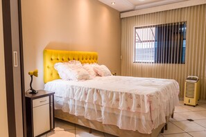 A bedroom with a yellow tufted headboard, a white floral bedspread, and a bedside table with a lamp.
