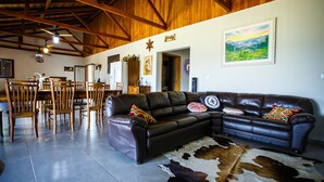 A spacious living room with a large leather sectional sofa, wooden dining table, and chairs. A cowhide rug is on the floor, and there is a painting on the wall.
