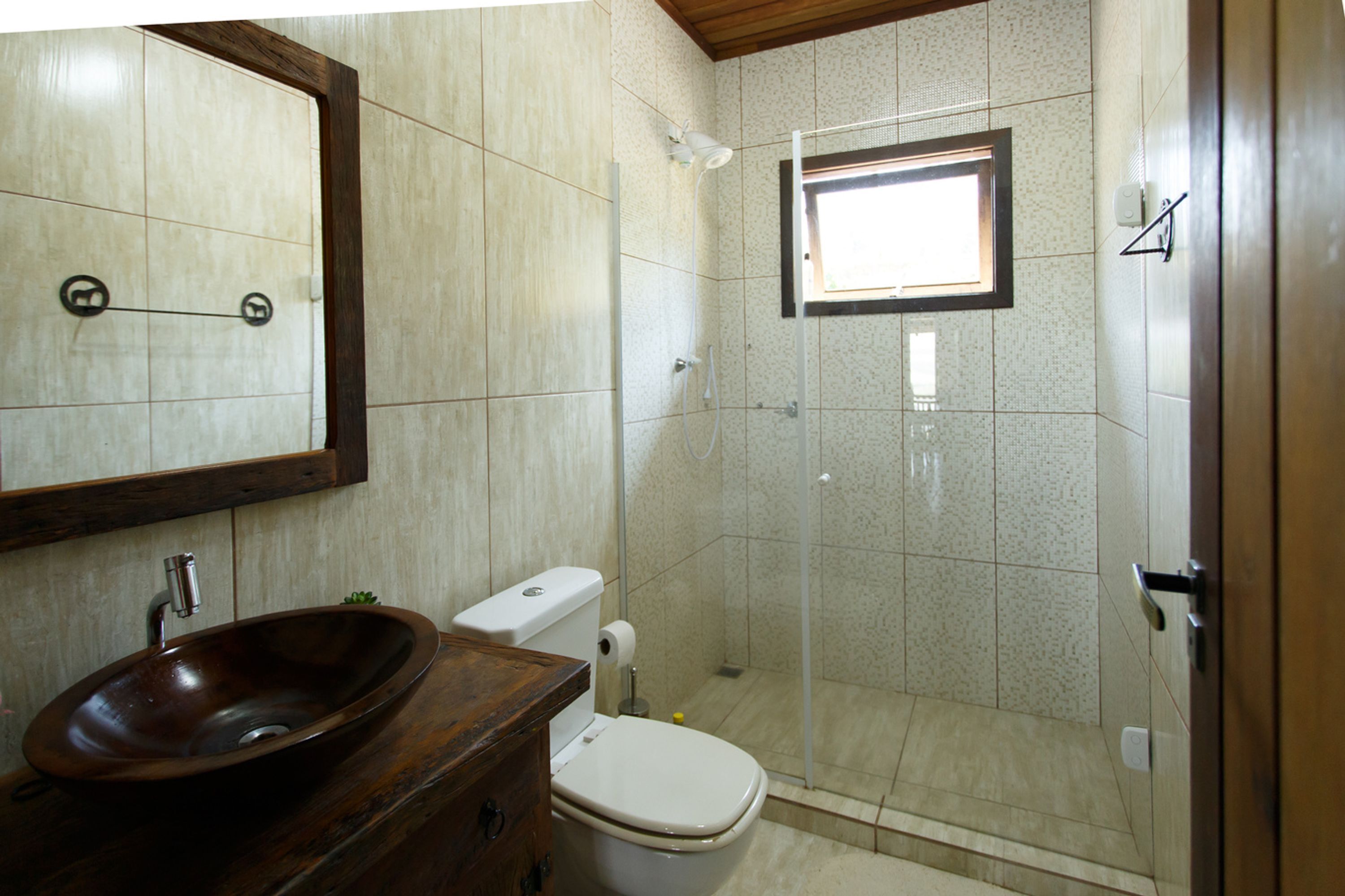 Un baño con tocador de madera, inodoro blanco, cabina de ducha de vidrio y un espejo grande.