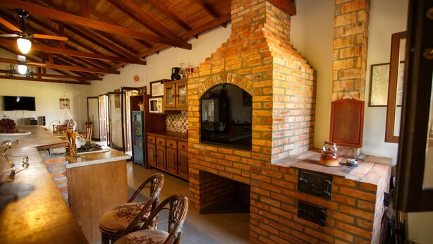 A kitchen with a brick oven, wooden ceiling beams, and a bar area with stools.