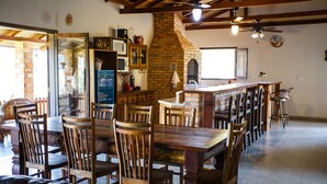 A spacious dining area with wooden tables and chairs, a brick oven, and a kitchen area with a sink and cabinets.