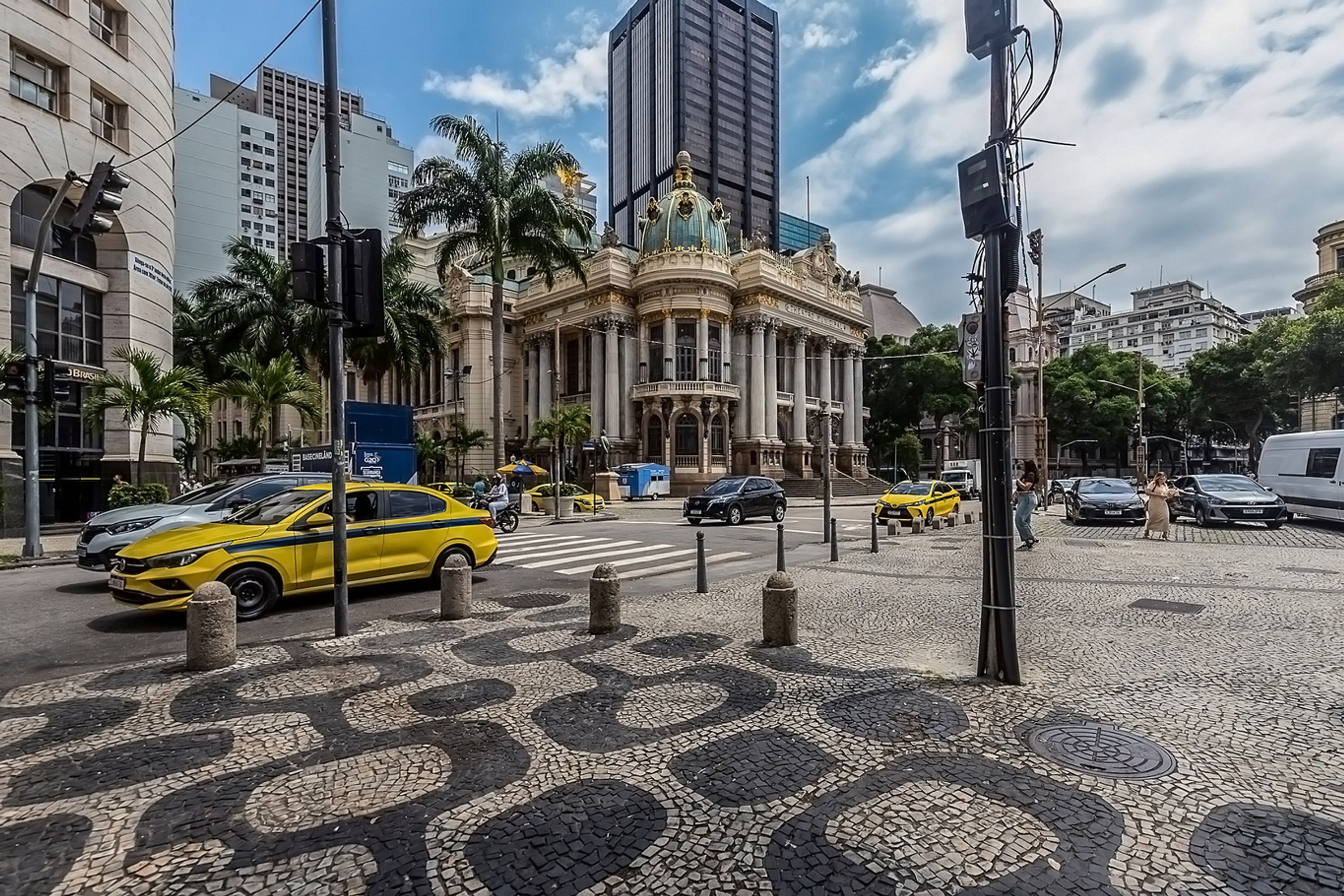 A historic building with classical architecture, a cobblestone plaza, and modern vehicles.