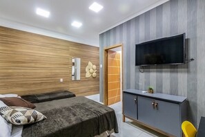 A modern bedroom with a wooden wall, a flat-screen TV, a cabinet, and a bed with a dark cover. - Loft pr x do Aeroporto no Centro e com Wi-fi (Rio de Janeiro)