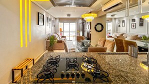 A modern kitchen with a gas stove, granite countertops, and a dining area with a glass table. - Timo Apto de Frente Para Praia do Boqueir o SP (Praia Grande)