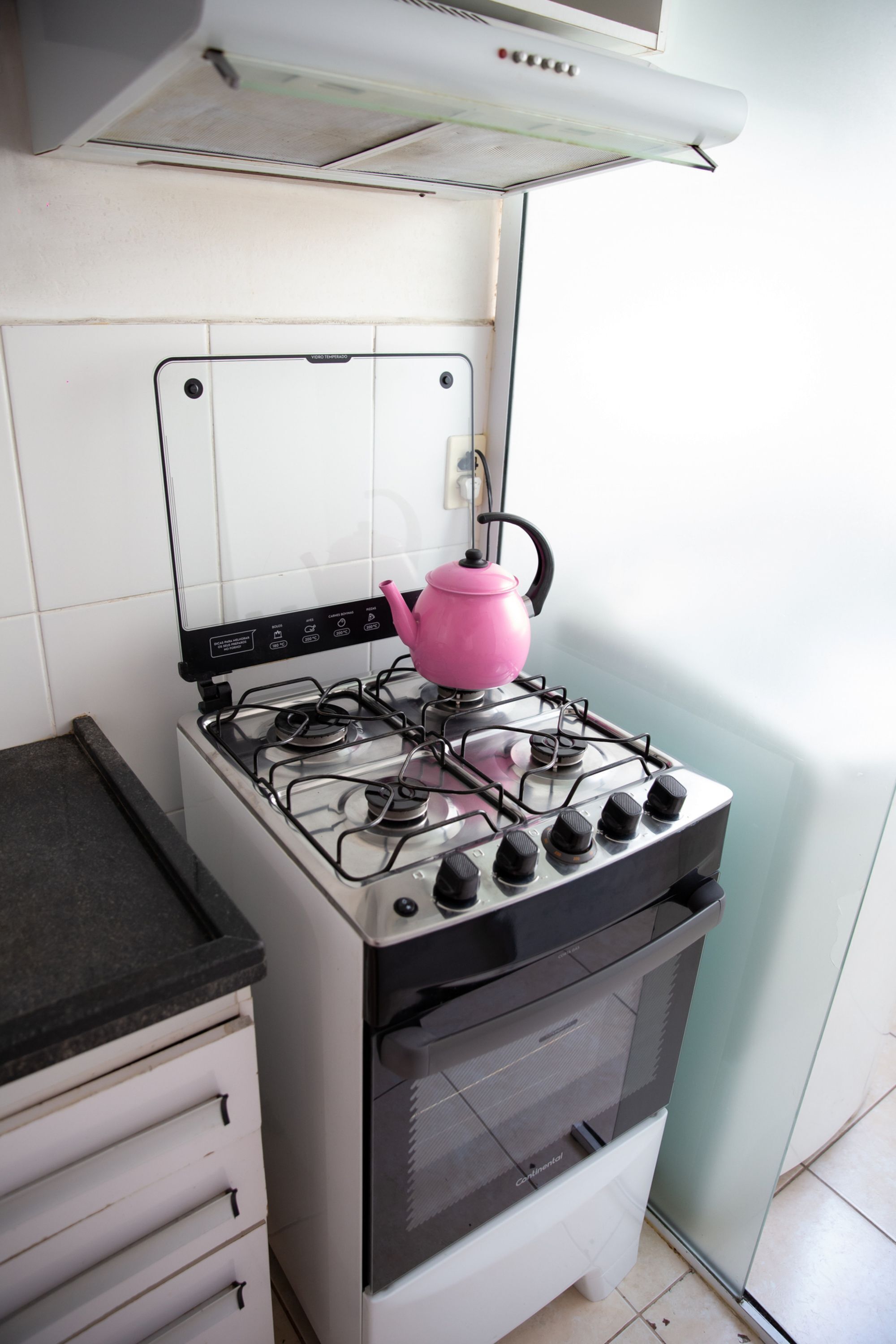 A kitchen with a gas stove, a pink kettle, and a white oven.