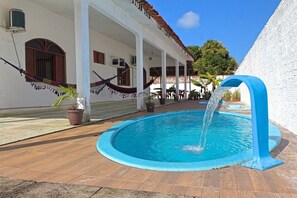 A pool with a blue fountain, surrounded by a wooden deck and a white building with columns and a tiled roof. - Casa c Piscina a 300m da Praia do Po o Cabedelo PB (Cabedelo)