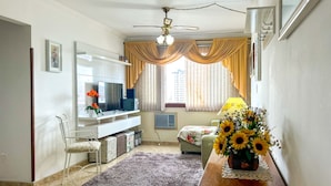 Ein Wohnzimmer mit Fernseher, Sofa und einem Tisch mit einer Vase voller Sonnenblumen.