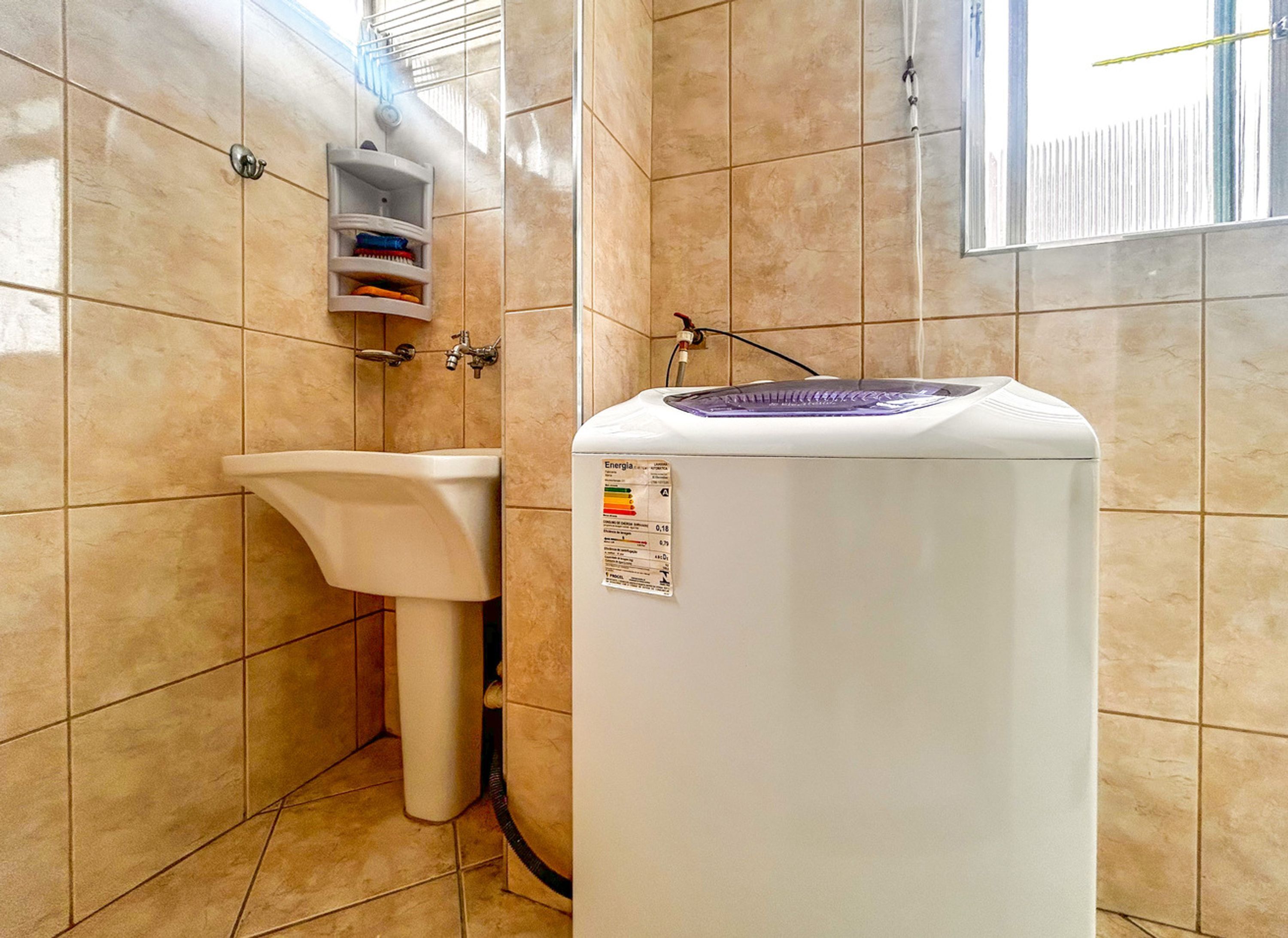 A bathroom with a white pedestal sink, a white water heater, and beige tiled walls.