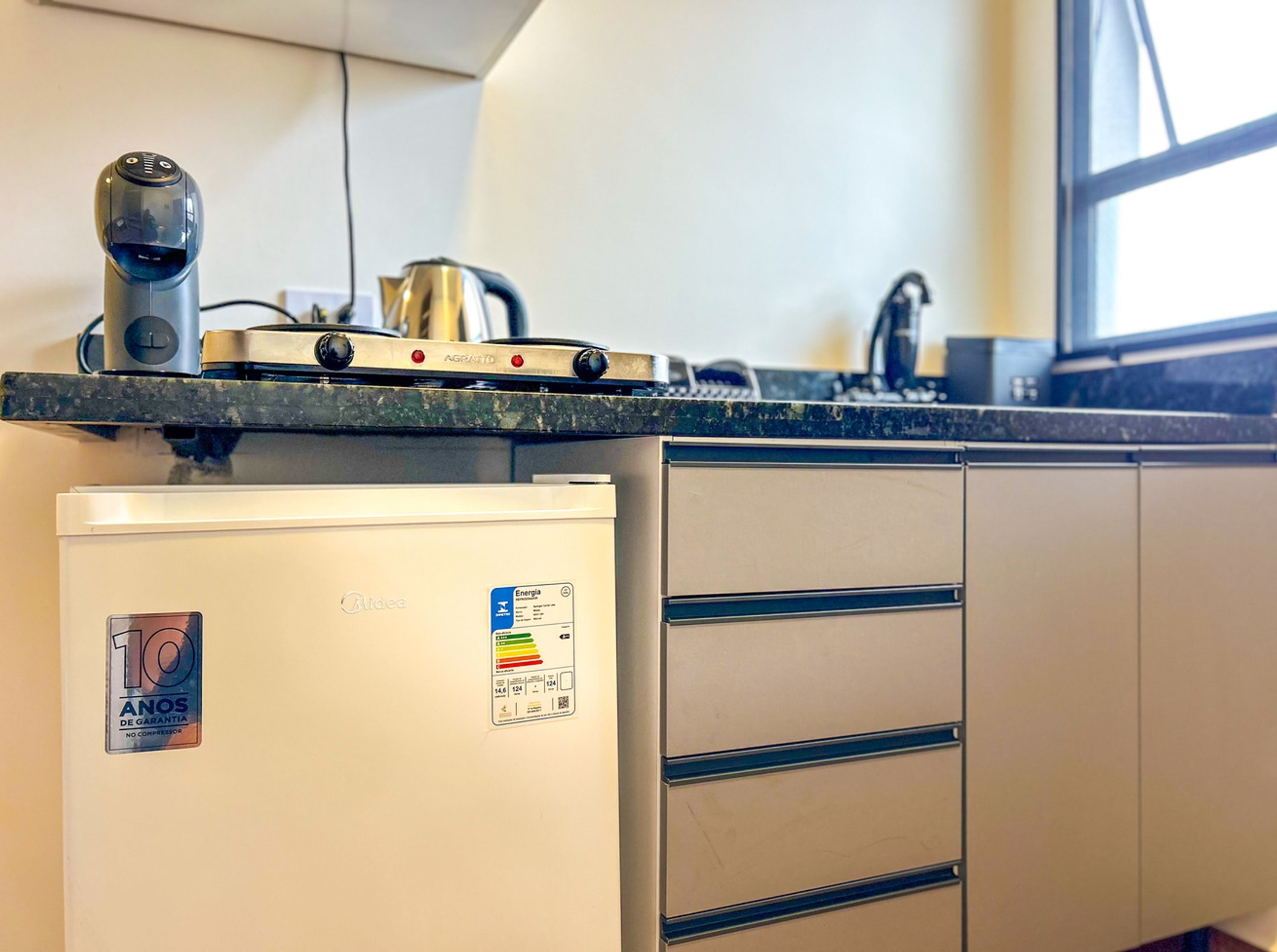 A kitchen with a compact refrigerator, a kettle, and a coffee machine on the countertop.