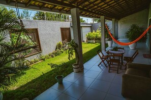 A covered patio with a tiled floor, a wooden table with chairs, a hammock, and potted plants.