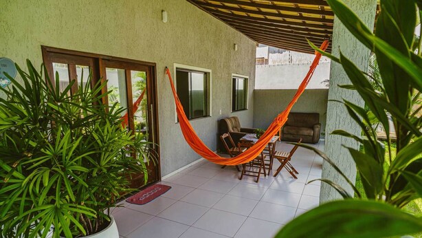 Eine Terrasse mit Hängematte, Esstisch und Stühlen. Übertöpfe und ein Fliesenboden sind ebenfalls vorhanden.