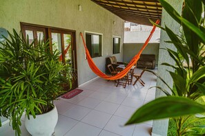 A patio area with a hammock, a dining table, and chairs. There are potted plants and a tiled floor.