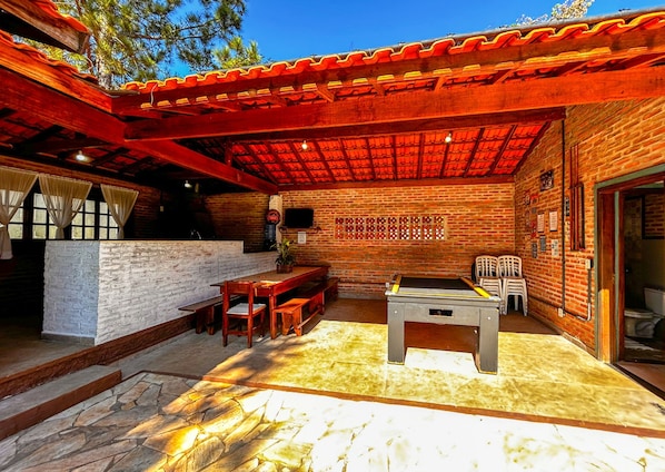 A covered outdoor patio with a brick wall, a table with chairs, and a bench. - Ch Cara com Piscina e Churrasq em Botucatu SP (Botucatu)