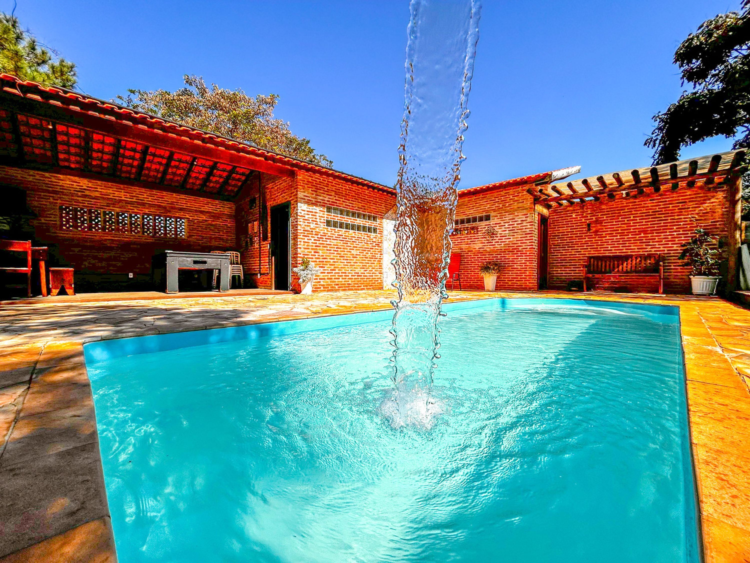Piscina com uma fonte no centro, rodeada por um edifício de tijolo com telhado vermelho e área de estar ao ar livre.