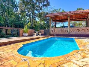 A rectangular swimming pool with a tiled deck, surrounded by a brick wall and a wooden pergola. - Ch Cara com Piscina e Churrasq em Botucatu SP (Botucatu)