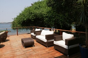 A wooden deck with wicker furniture and a view of the water. - Chal com Vista e Acesso ao Rio Grande - MG (Delfinopolis)