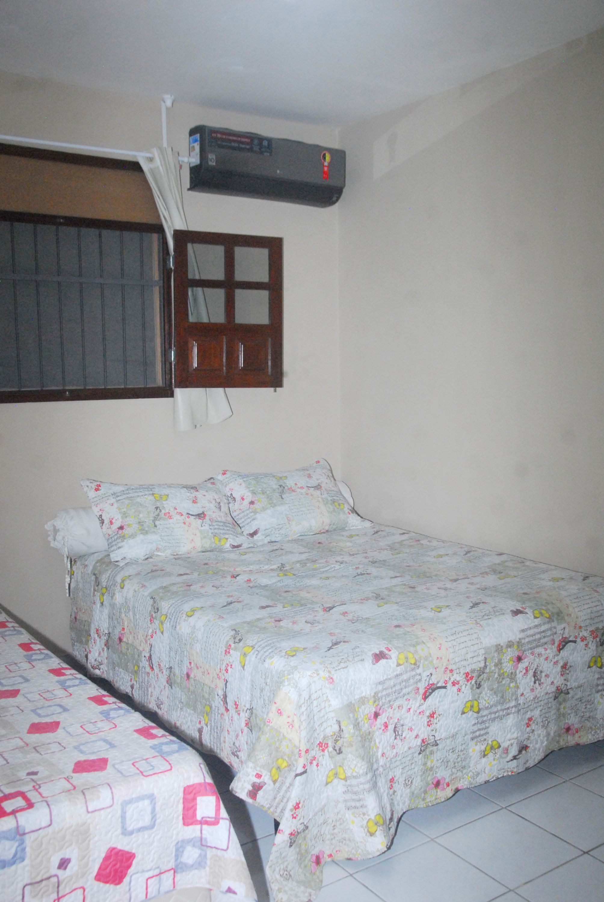 A bedroom with two beds, a window with bars, and an air conditioner mounted on the wall.