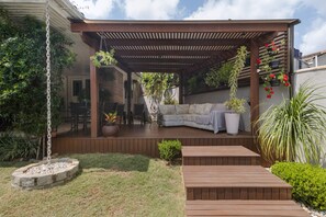 A covered patio area with a wooden deck, a cushioned seating area, and potted plants. - Casa com Piscina Churrasq e Wi-fi em Crici ma SC (Criciuma)