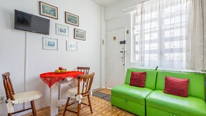 A room with a dining table, chairs, a green sofa, and a TV mounted on the wall. - Timo Apto com Wi-fi a 350m da Praia de Copacabana (Rio de Janeiro)