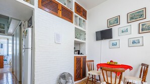 A compact living space with a dining area, a TV mounted on the wall, and a refrigerator. - Timo Apto com Wi-fi a 350m da Praia de Copacabana (Rio de Janeiro)