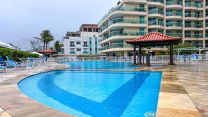 A swimming pool with lounge chairs and a gazebo, surrounded by a multi-story hotel building with balconies.