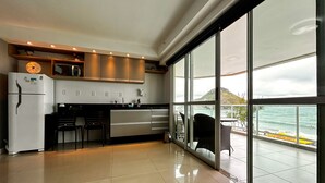 A modern kitchen with a large sliding glass door leading to a balcony with a view of the ocean.