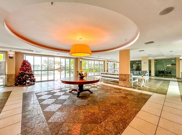 Un vestíbulo amplio con un gran árbol de Navidad, una mesa redonda con un florero y vistas al exterior a través de amplias ventanas.