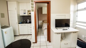 Een kleine kamer met een kitchenette, een bed, een televisie en een bureau.