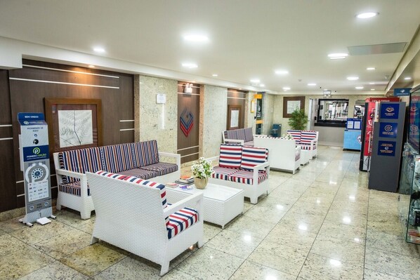 A hotel lobby with seating areas, a reception desk, and a digital information kiosk. - Apto p Home Office c boa Localiza o - Asa Sul DF (Brasília)