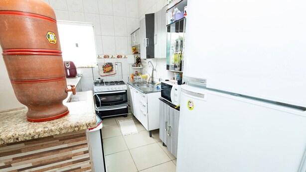 Une cuisine équipée d’un grand pot en terre cuite, d’une cuisinière, d’un four, d’un four à micro-ondes et de meubles de rangement blancs.