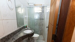 Une salle de bain avec un lavabo sur un plan de toilette en granit, des toilettes et une douche dotée d’une porte en verre.