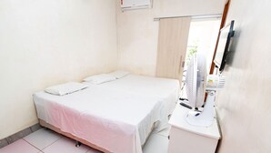 Une petite pièce propre, avec un lit simple, un bureau équipé d’un ordinateur et une fenêtre avec des rideaux.