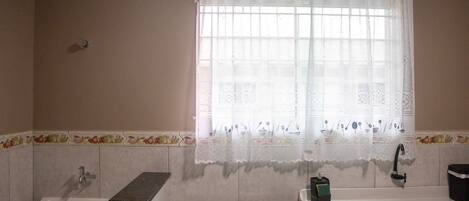 A kitchen with a gas stove, sink, and window with lace curtains.