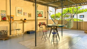 A covered patio area with a table and chairs, artwork on the walls, and a view of greenery outside. - Timo Apto 350m da Praia de Copacabana RJ (Rio de Janeiro)