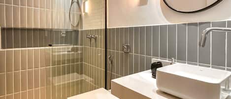 A modern bathroom with a glass-enclosed shower, a white sink, and a large mirror.