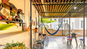 An outdoor patio with a hammock, chairs, and tables. There are plants and a metal cage with eggs. - Timo Apto 350m da Praia de Copacabana RJ (Rio de Janeiro)