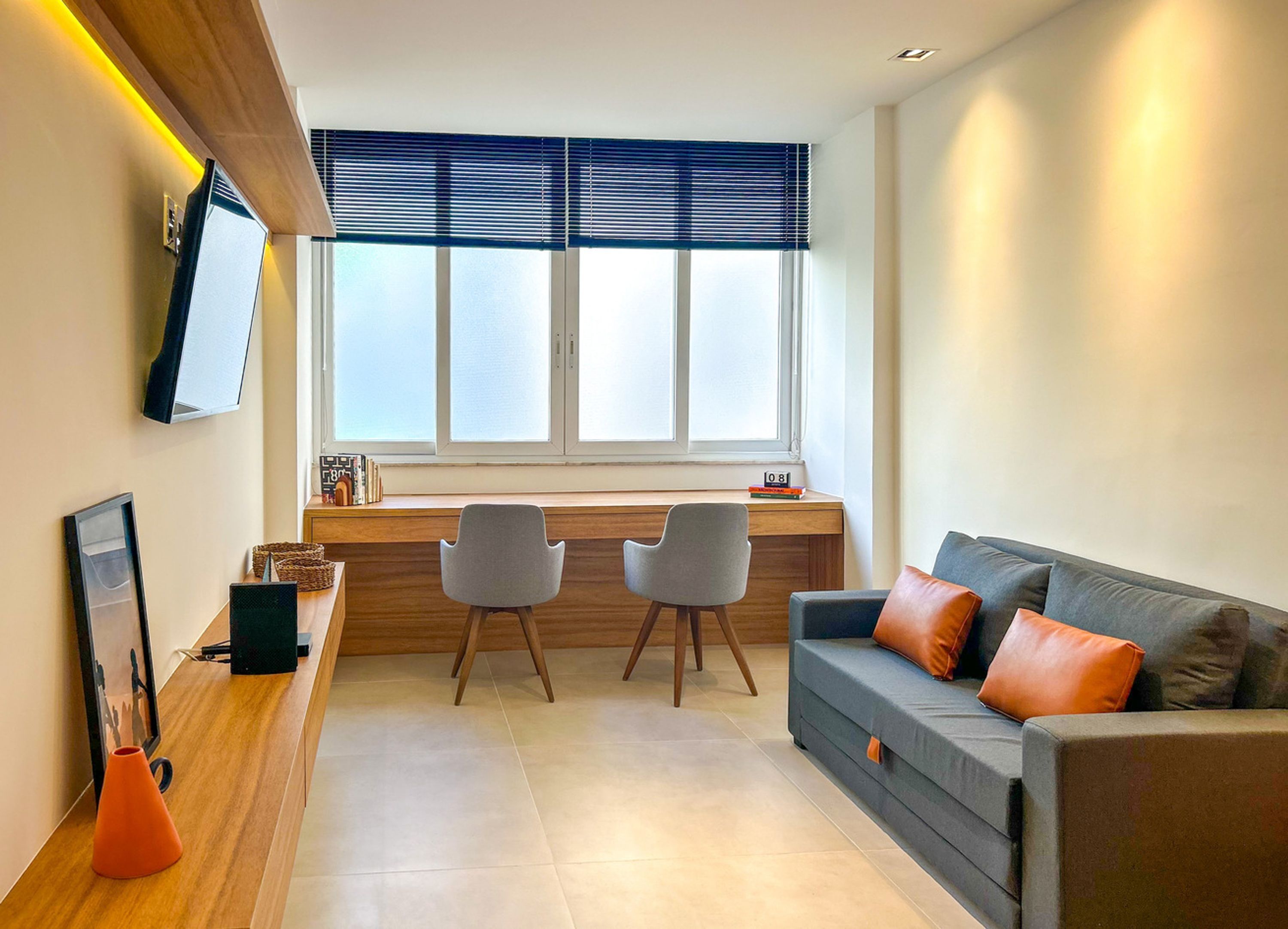A modern living room with a sofa, two chairs, a wooden desk, and a TV mounted on the wall.