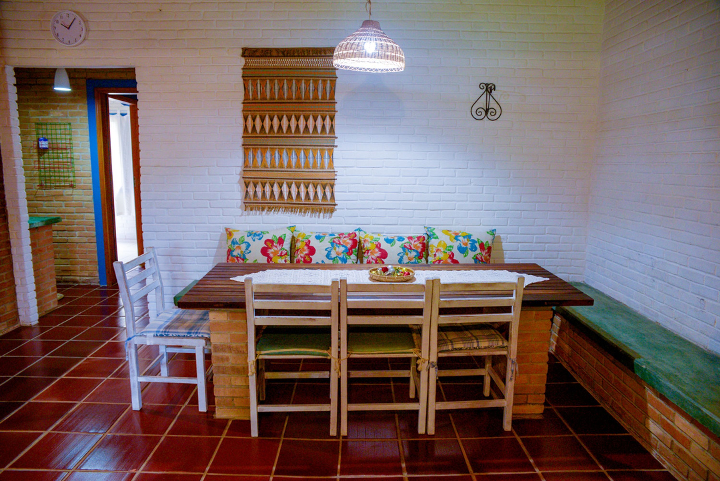 A dining area with a wooden table and chairs, a bench with a floral cushion, a hanging light fixture, and a wall clock.