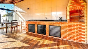 A kitchen with a brick oven, tiled walls, and a wooden ceiling. - Casa a Poucos Metros da Praia do Coral - Cabo Frio (Cabo Frio)
