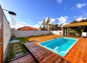 Une piscine avec une terrasse en bois, un patio couvert et une vue sur un immeuble résidentiel dont le toit est recouvert de tuiles rouges.