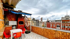 A rooftop patio with a brick oven, red chairs, and a tiled floor. - Apto a 800m da Praia da Enseada no Guaruj SP (Guarujá)
