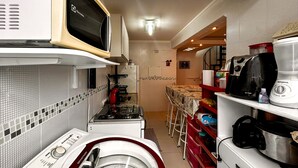 A compact kitchen with a washing machine, microwave, and a coffee maker. - Apto a 800m da Praia da Enseada no Guaruj SP (Guarujá)