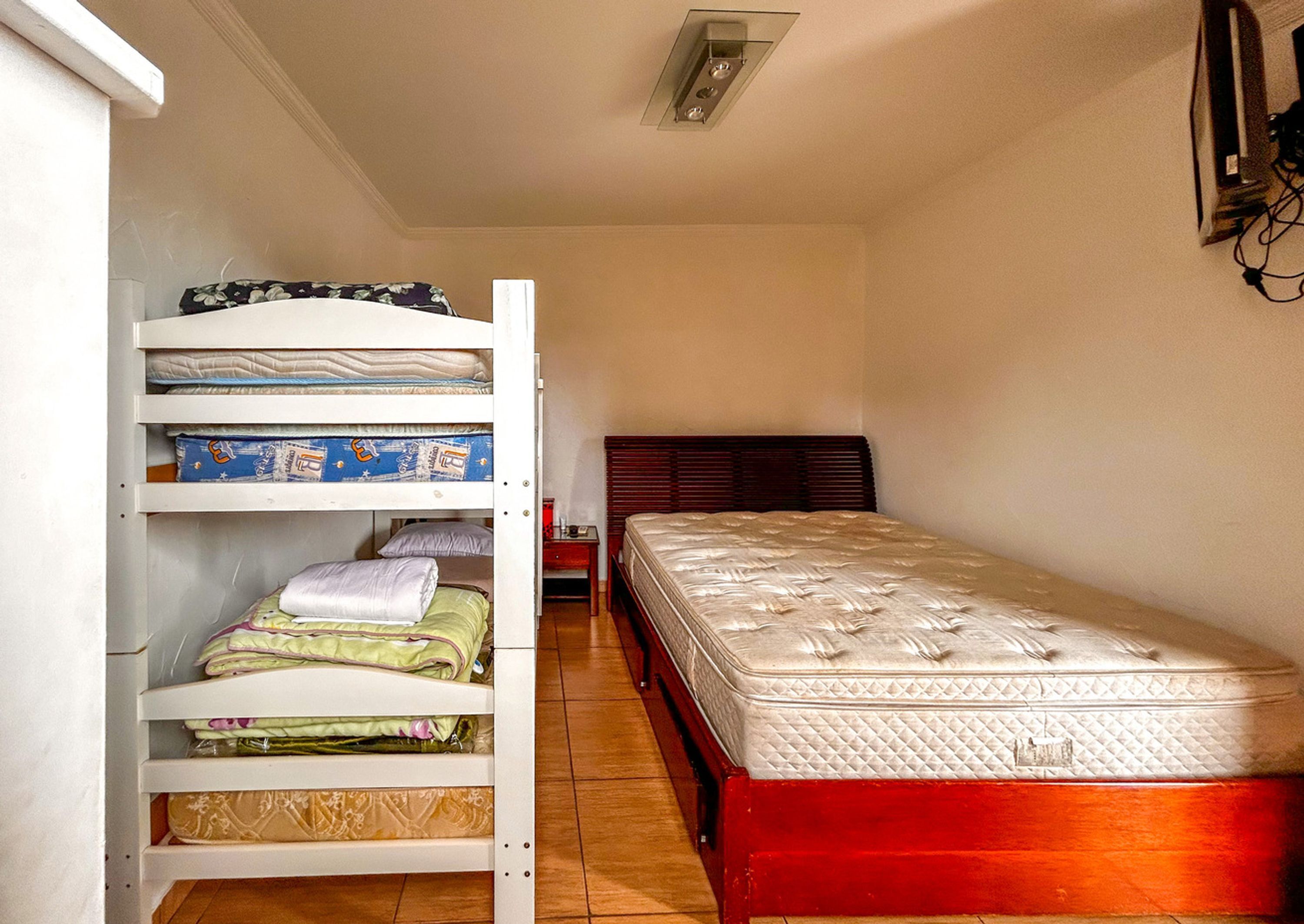 A compact room with a bunk bed, a single bed, and a small bedside table.