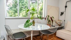A dining area with a round table, two wireframe chairs, a vase with plants, a globe, and a lamp on a white wall. - Apto com Excelente Localiza o em Asa Sul DF (Brasília)
