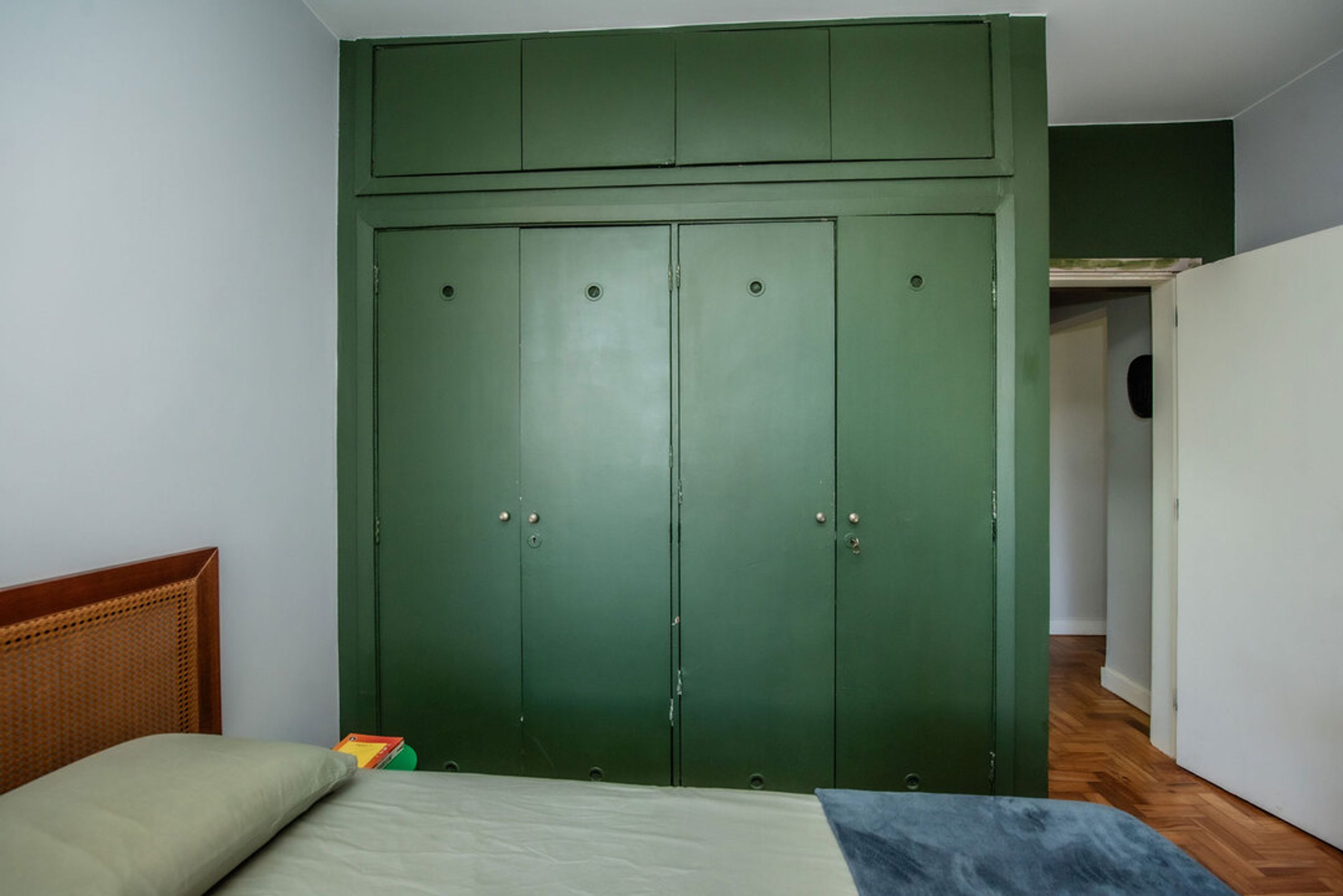 A bedroom with a green wardrobe, a wooden headboard, and a bed with a blue blanket.