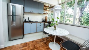 A modern kitchen with a stainless steel refrigerator, grey cabinets, a round marble table, and a view of greenery through large windows. - Apto com Excelente Localiza o em Asa Sul DF (Brasília)